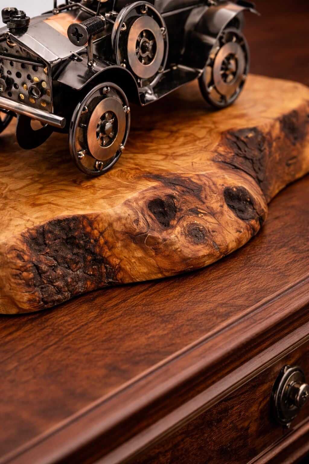 Side angle view of a rustic metal vintage car olive wood sculpture on a polished table.